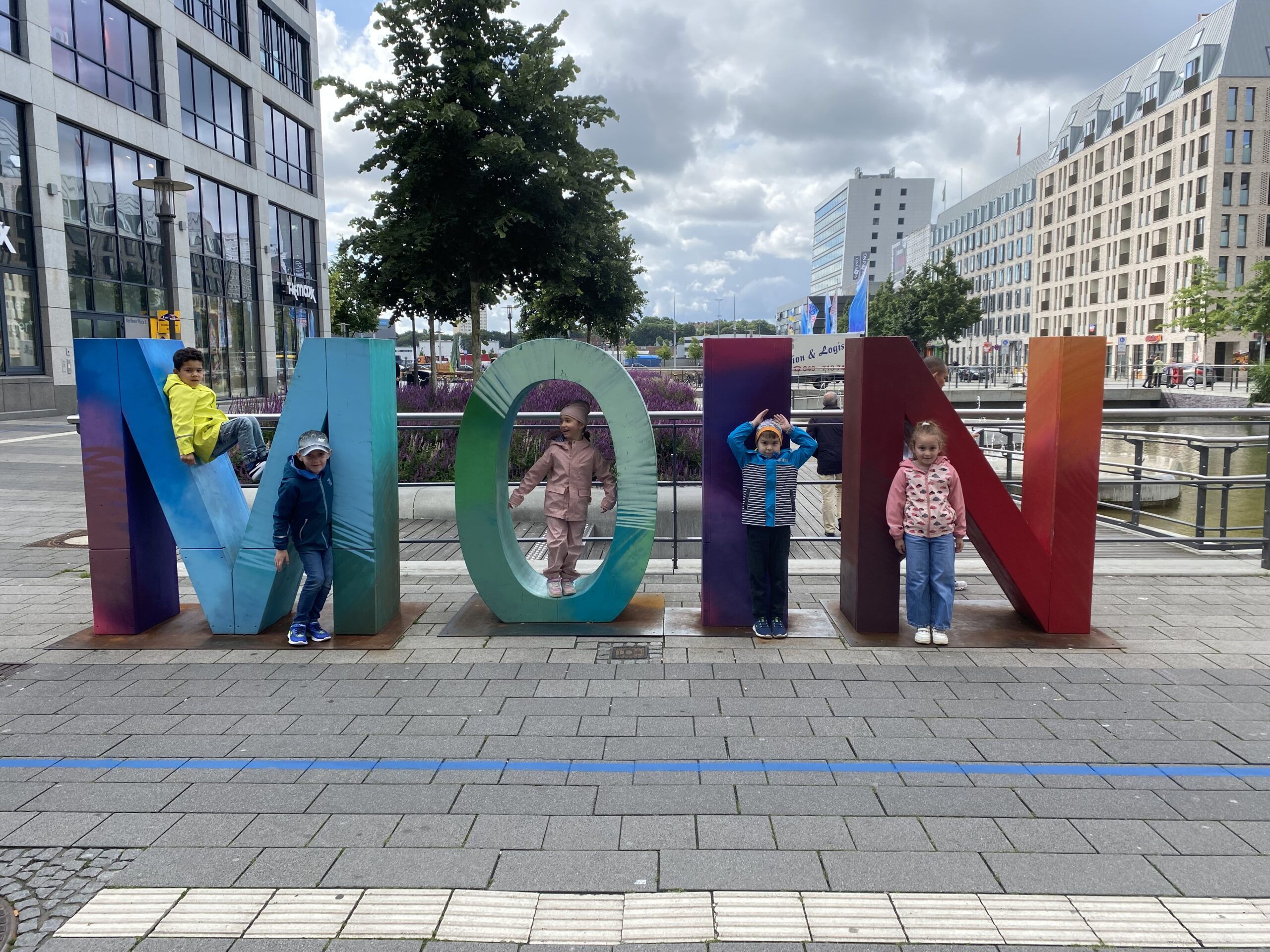 Die Buchstaben "MOIN" stehen als Touristenattraktion auf dem Boden. Kinder haben sich vor- und in den Buchstabne positioniert und posen für ein Foto.